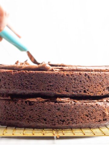 A hand spreading frosting onto the top of the stacked cake layers.