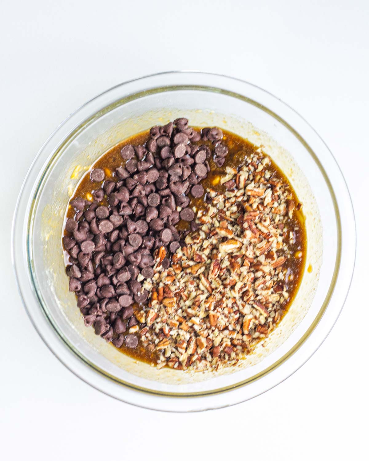 Chocolate chips and chopped pecans added to the pie filling in a clear glass mixing bowl.