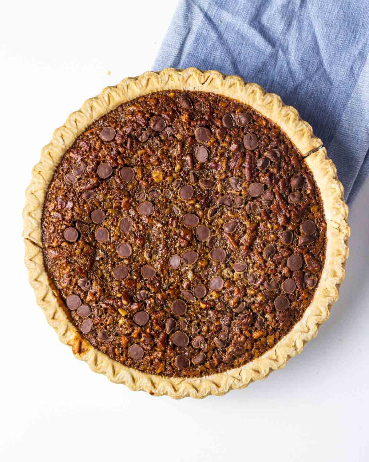 A baked maple bourbon chocolate pecan pie on a blue linen.