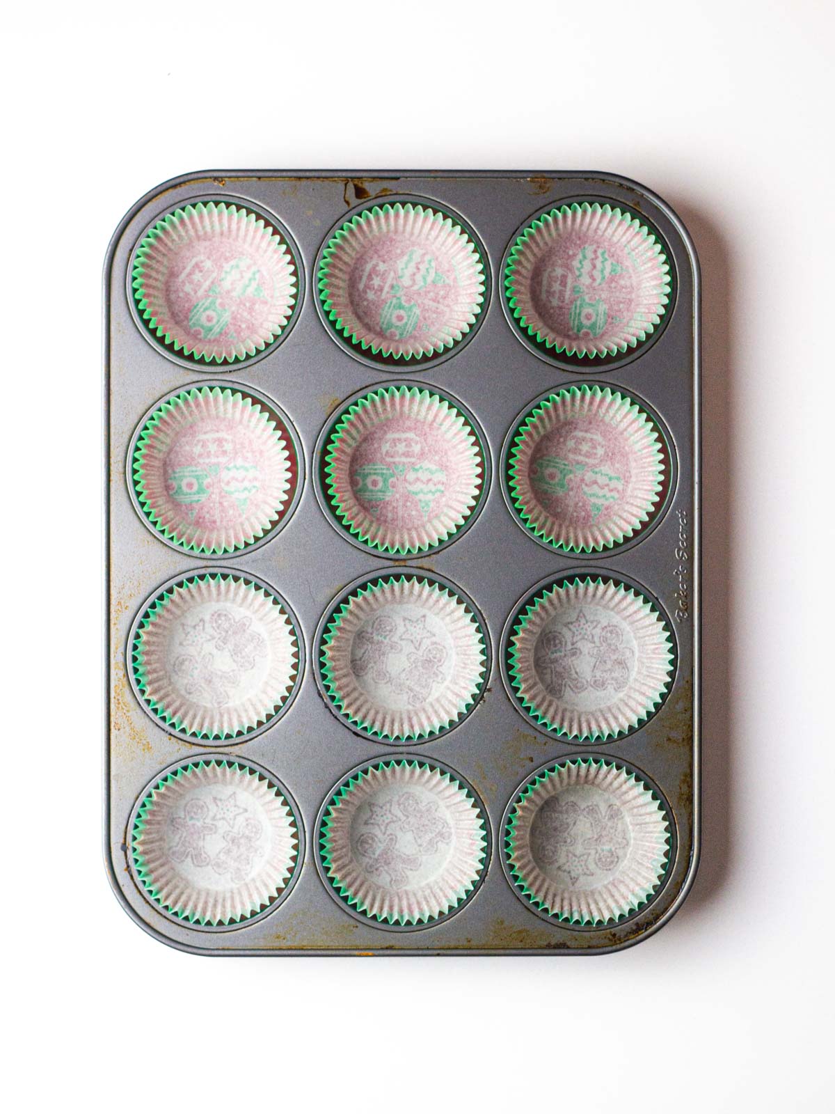 A 12-cup muffin pan lined with christmas themed paper liners.