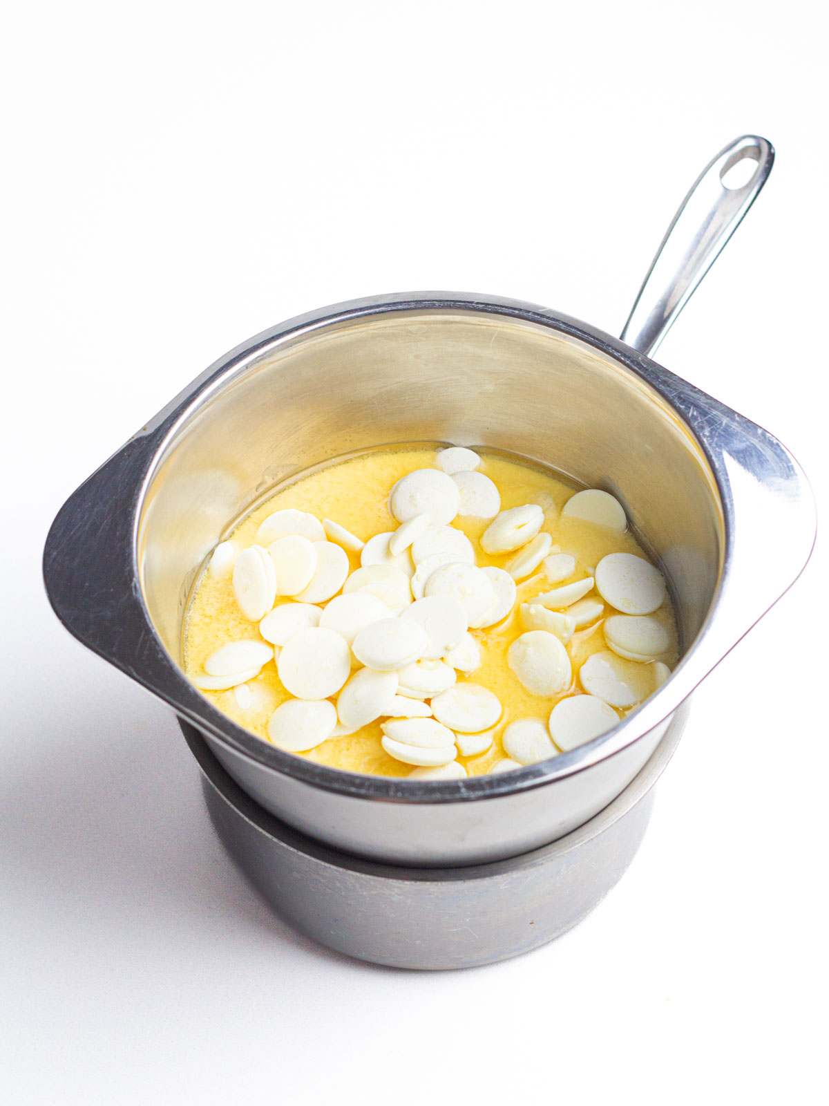 Vanilla melts, bourbon, and eggnog in a silver bowl on top of a saucepan to create a double boiler.