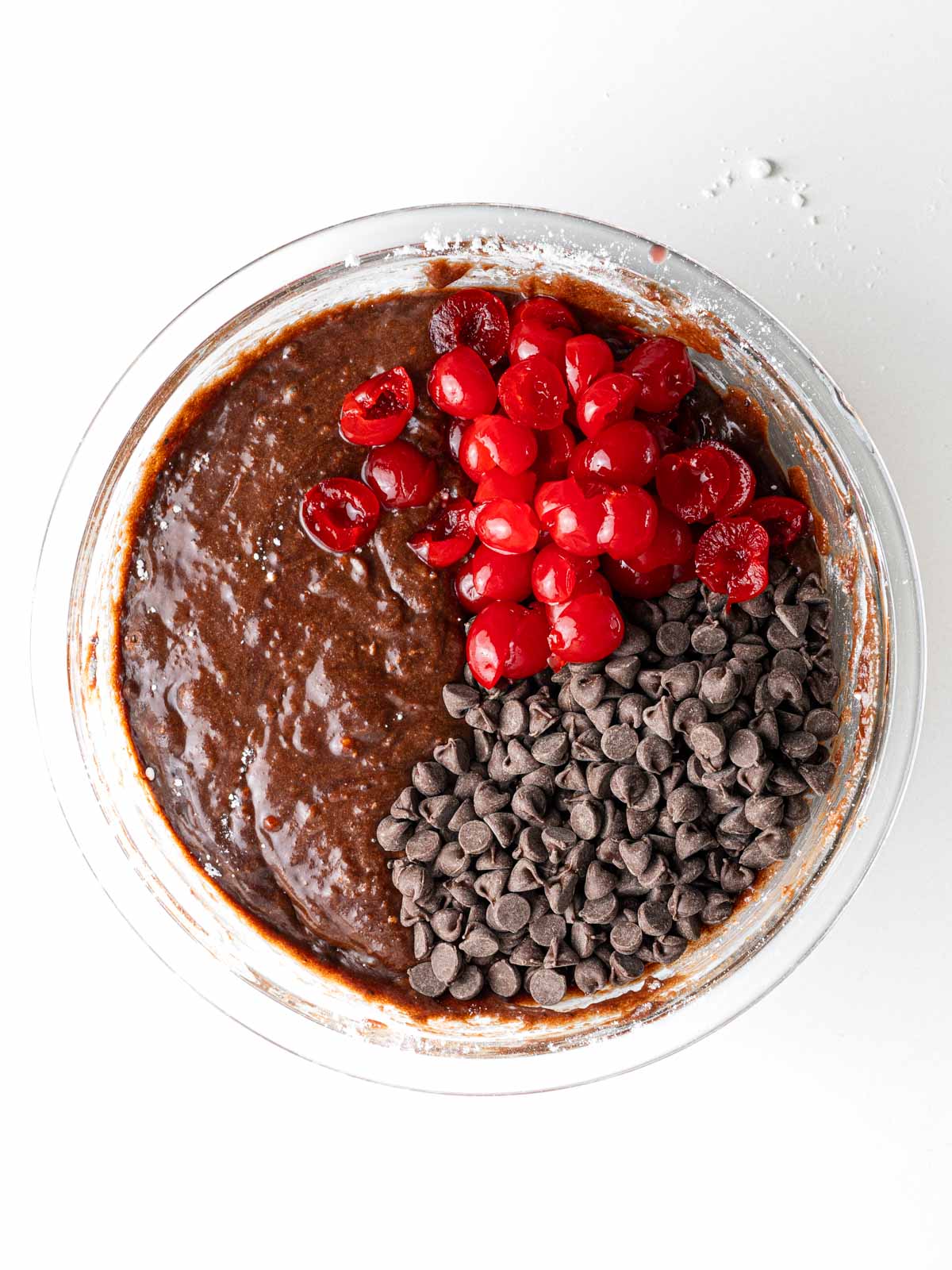Maraschino cherries and chocolate chips on top of the brownie batter in the clear glass mixing bowl.
