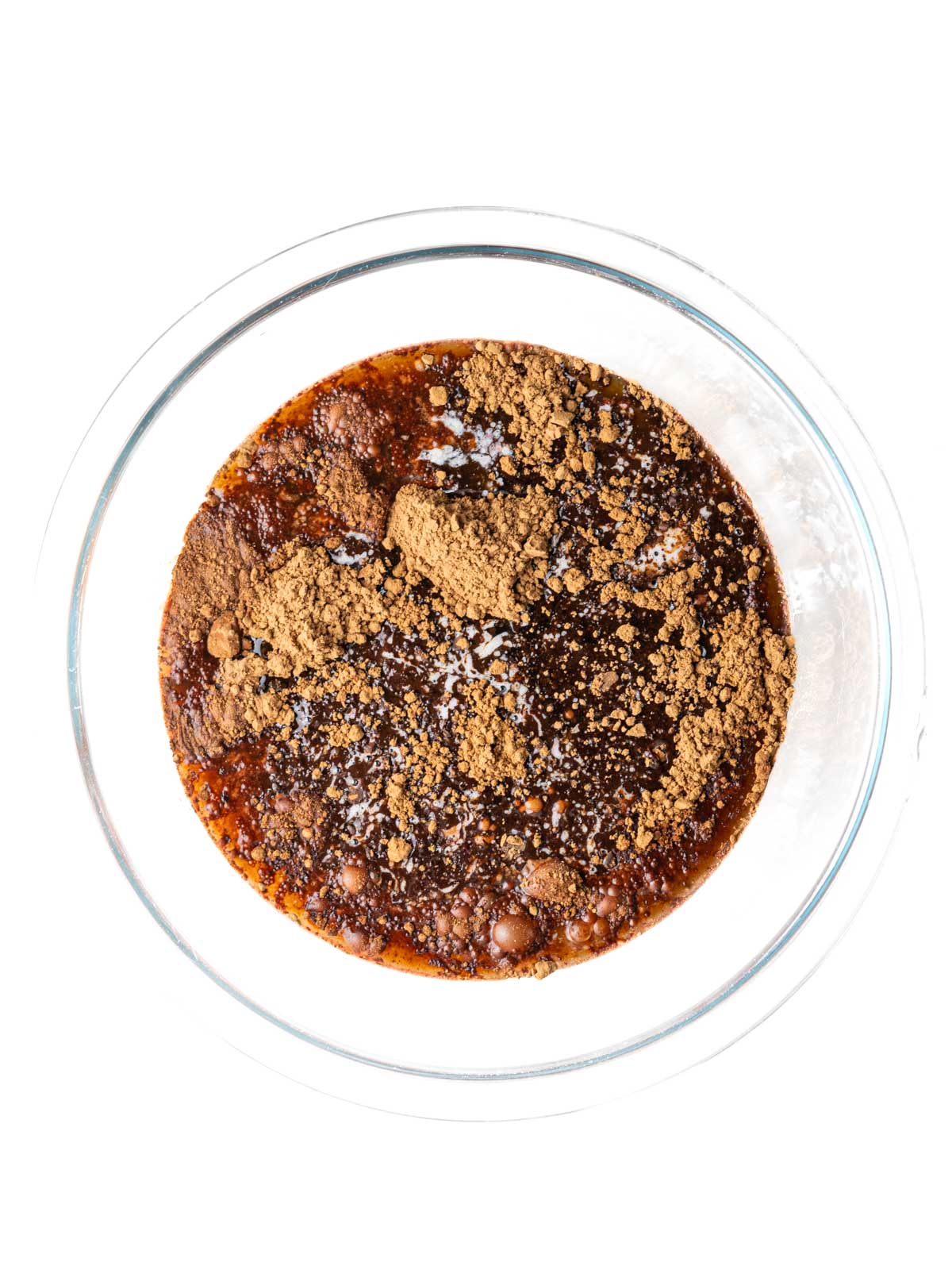 Cocoa powder, cherry juice, oil, and melted butter in a clear glass mixing bowl.