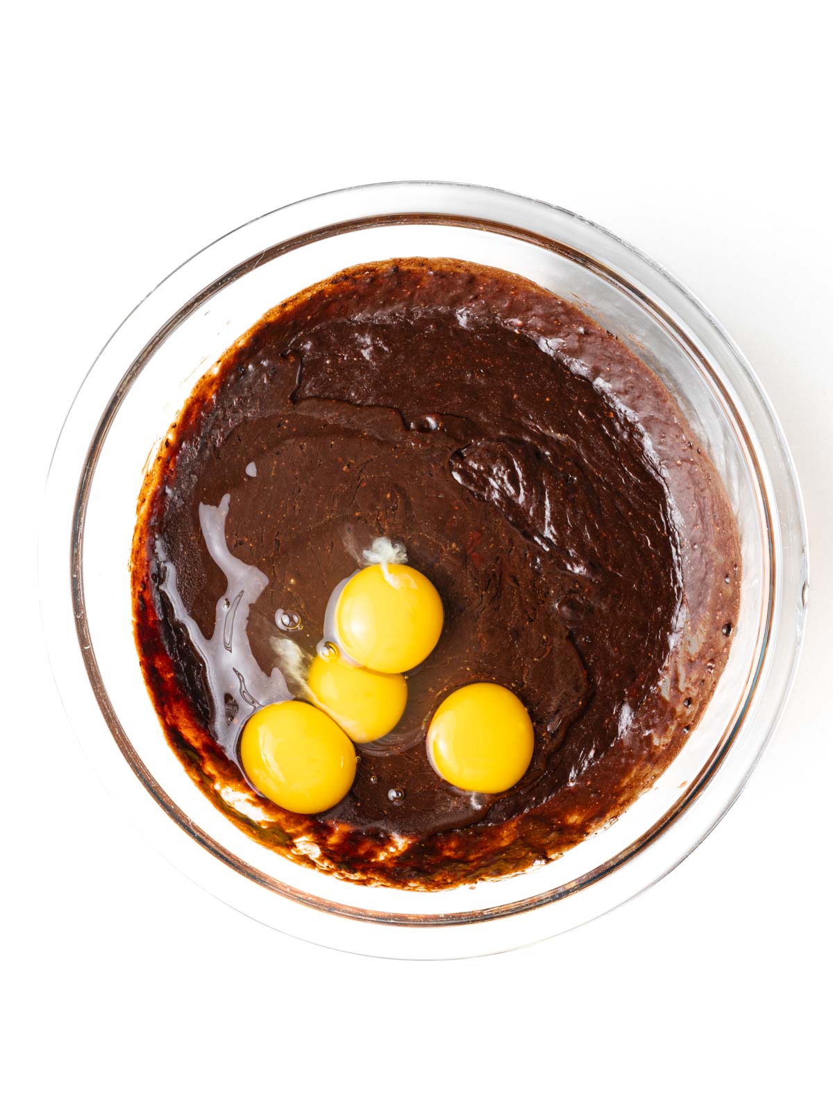 Eggs added to the brownie batter in a clear glass mixing bowl.