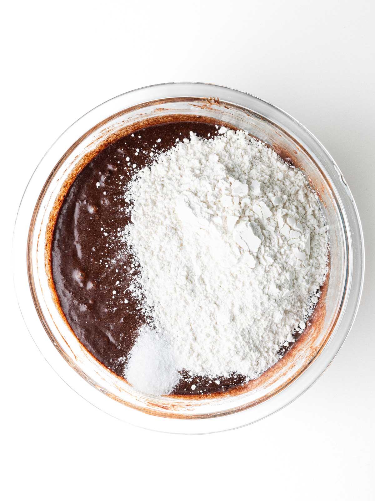 Flour and salt added to the brownie batter in a clear glass mixing bowl.