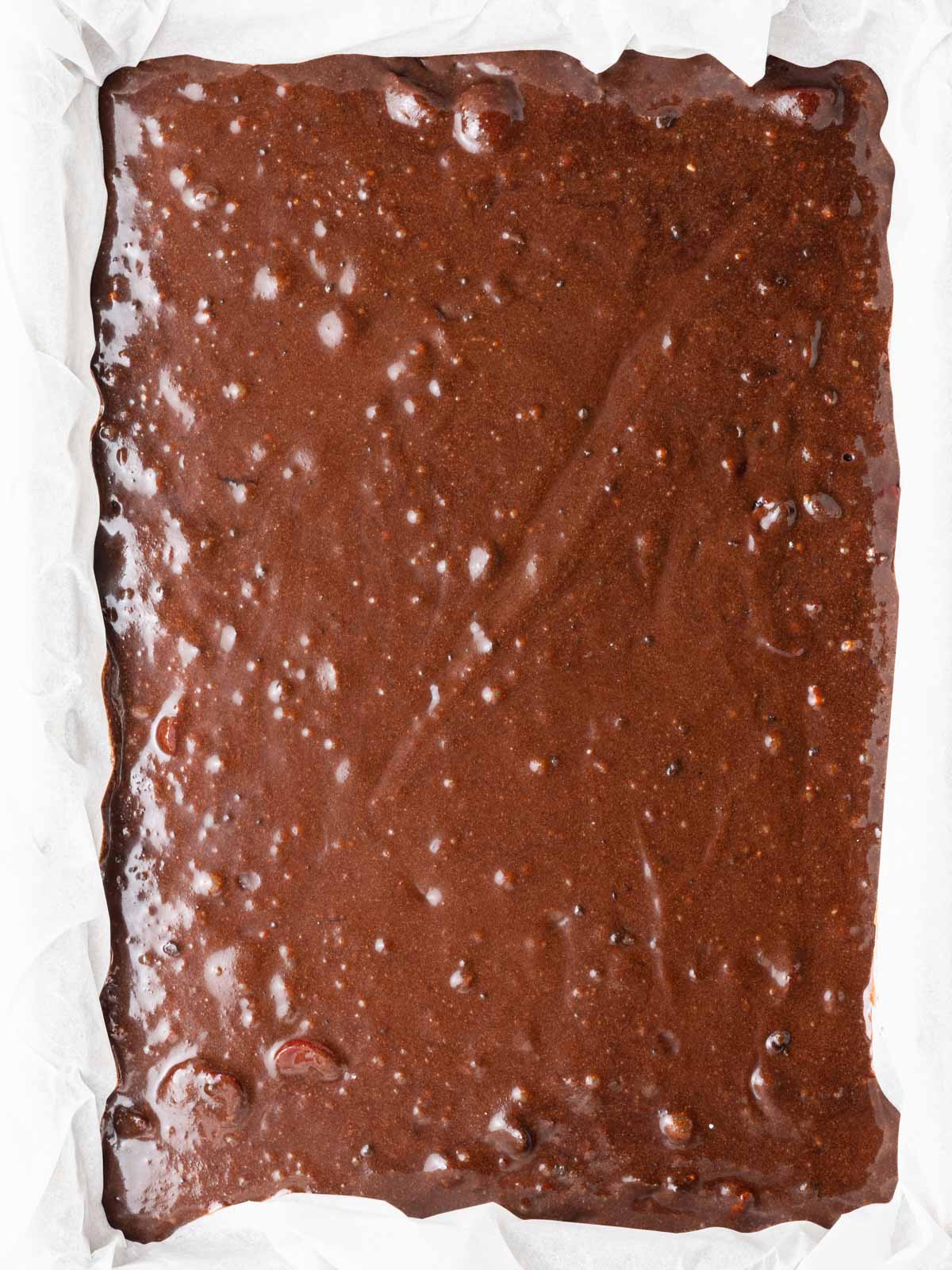 Unbaked chocolate cherry brownie batter in a 9x13 baking dish.