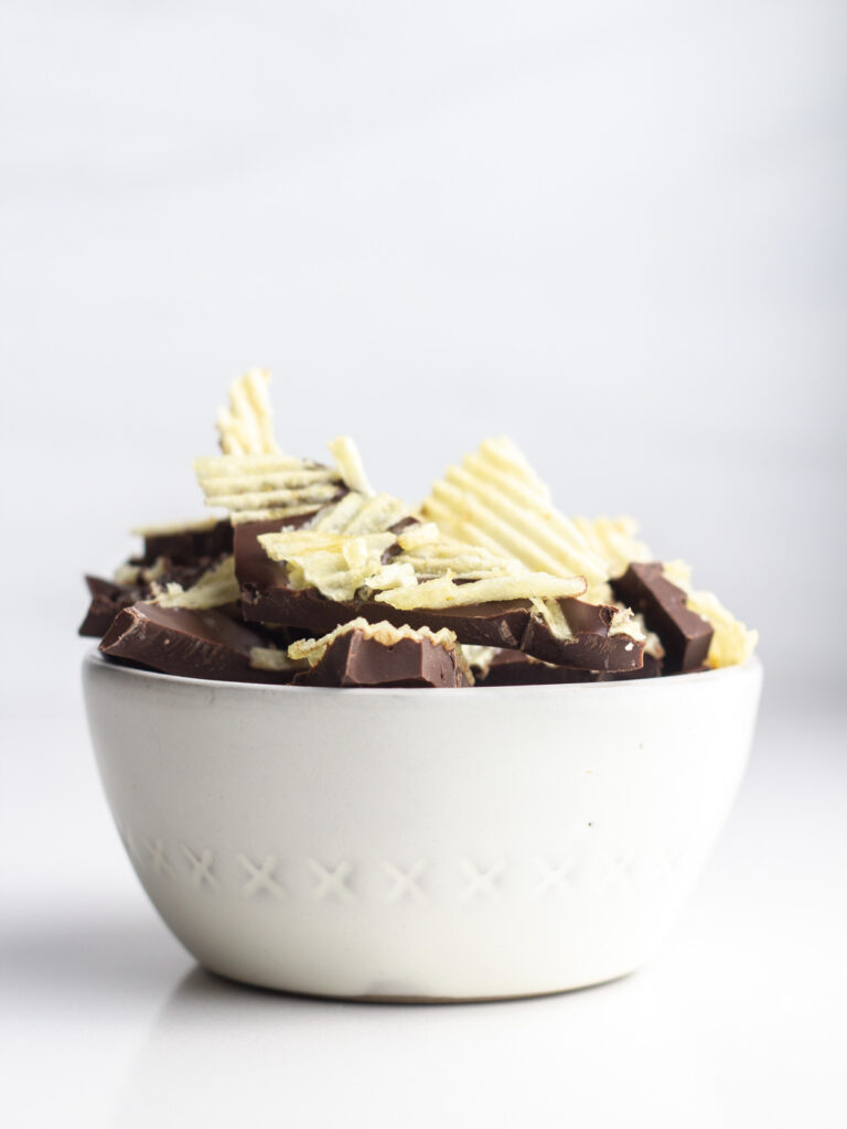A white bowl filled with potato chip topped chocolate bark.