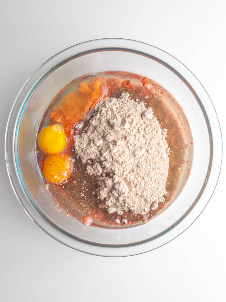 A glass bowl filled with the three red velvet brownie ingredients, unmixed.