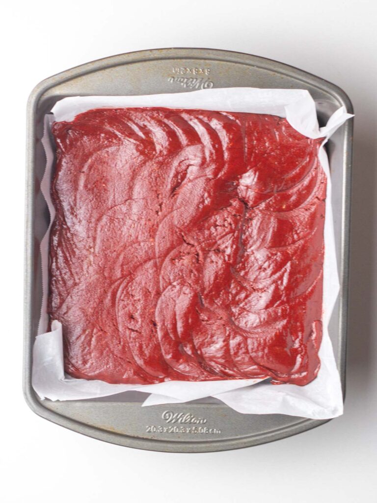 Red velvet brownie batter in a parchment lined 8x8 pan.