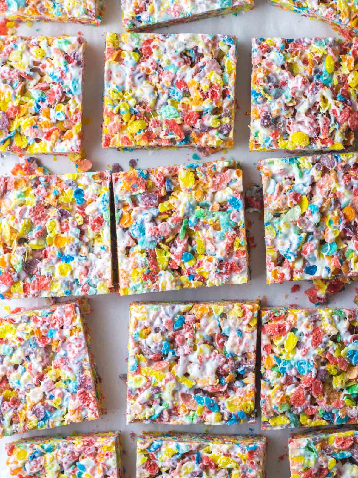 Squares of Fruity Pebbles bars slightly separated on a sheet of parchment.