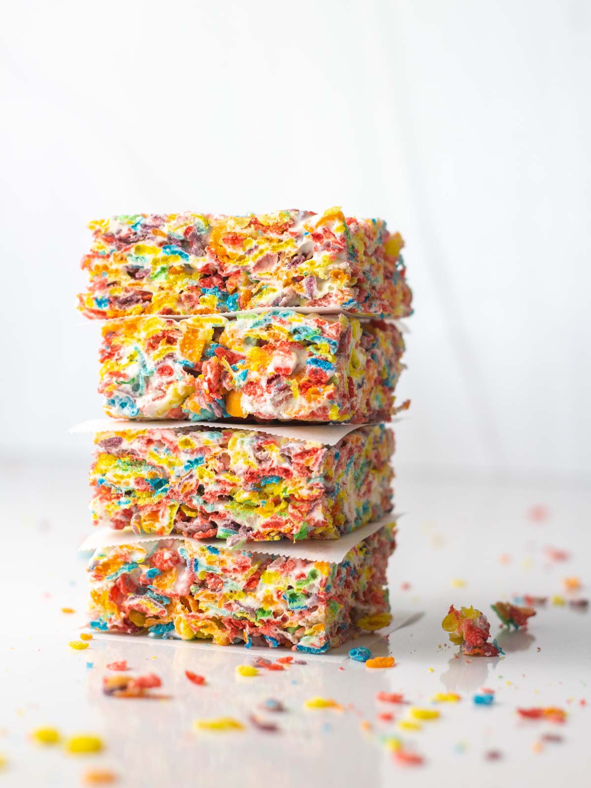 A stack of 4 Fruity Pebbles Bars each separated by a square of parchment paper.