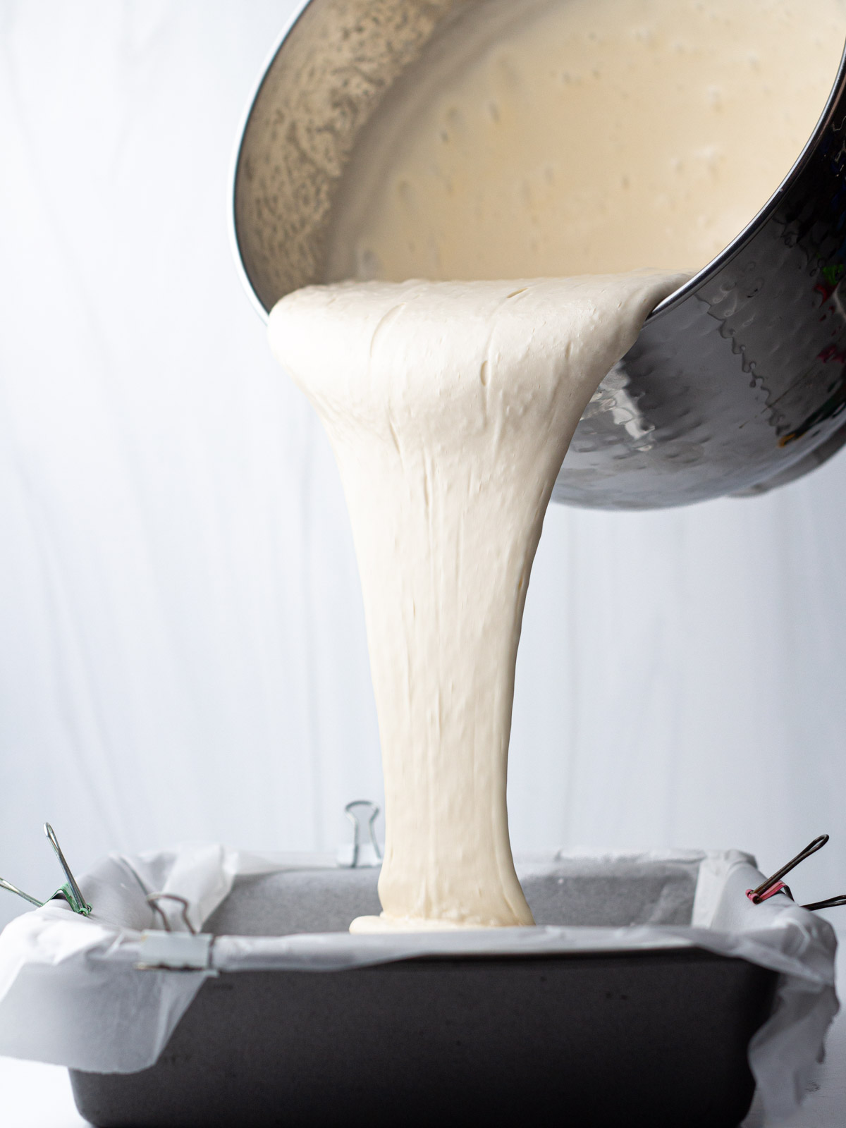 Caramel marshmallow mixture pouring from a silver mixing bowl into a parchment lined pan.