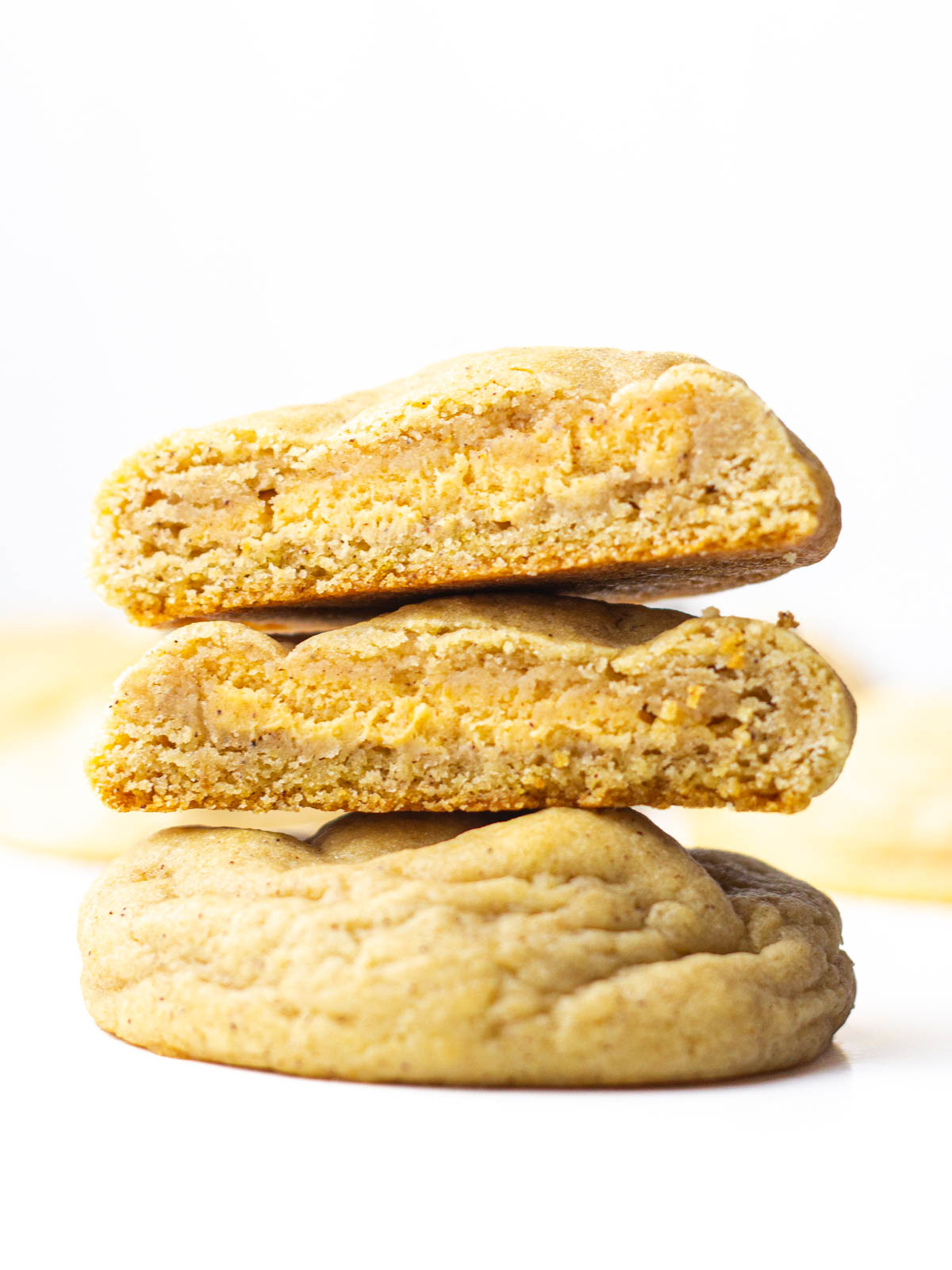 A cookie cut in half with the pumpkin cheesecake filling of both halves stacked on top of each other facing out, stacked on top of a whole Pumpkin Cheesecake Cookie.