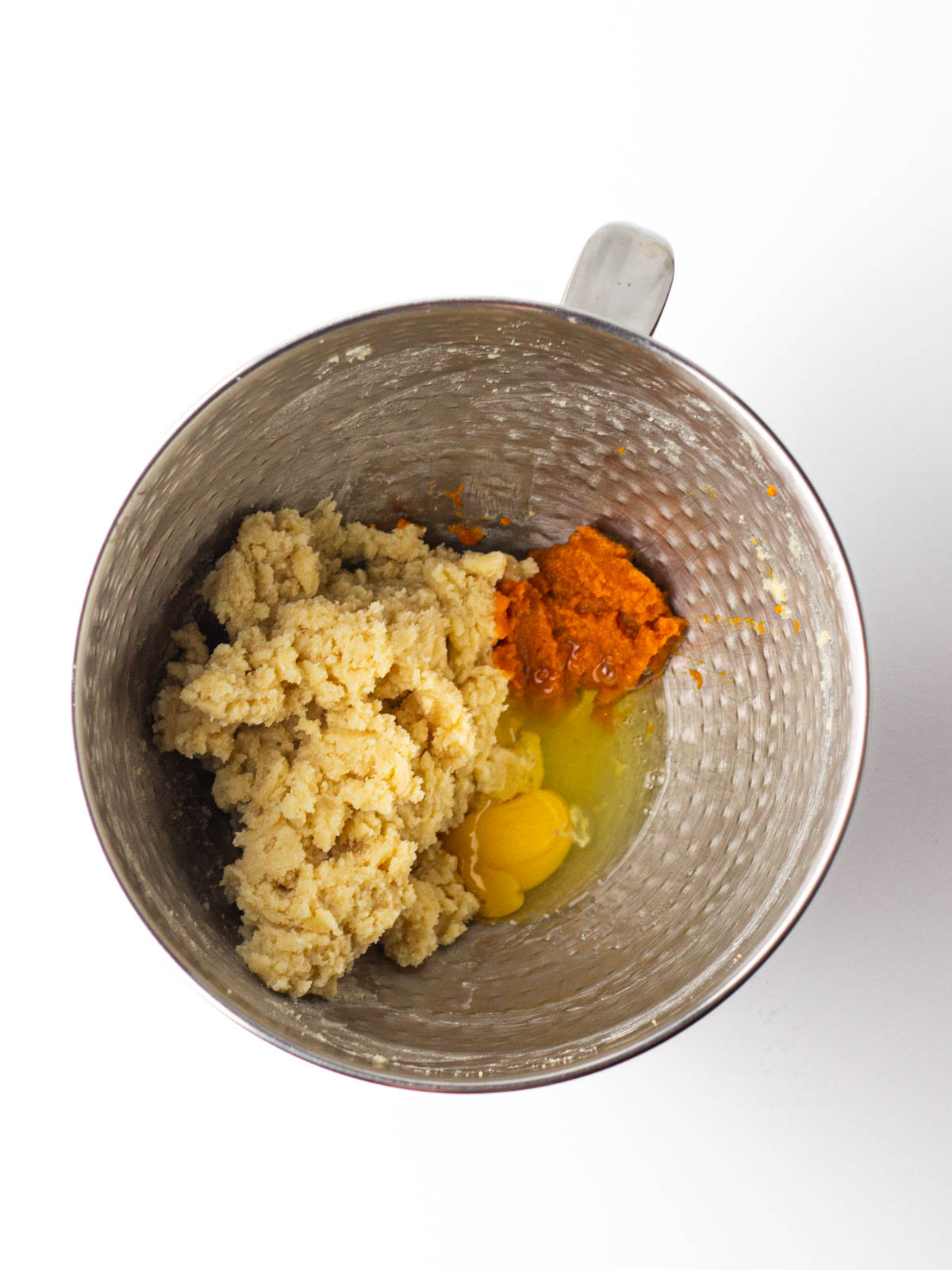 Egg and pumpkin added to cookie dough base in the textured silver mixing bowl.
