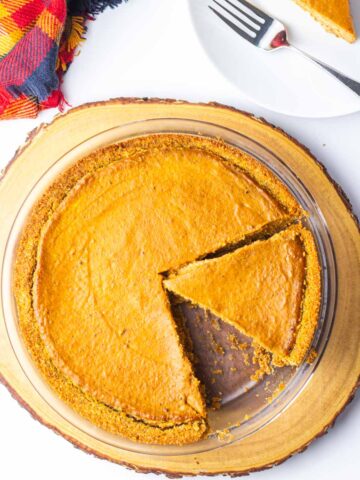 A pumpkin pie with one slice removed on a plate in the upper right corner and a second slice cut but not yet removed.