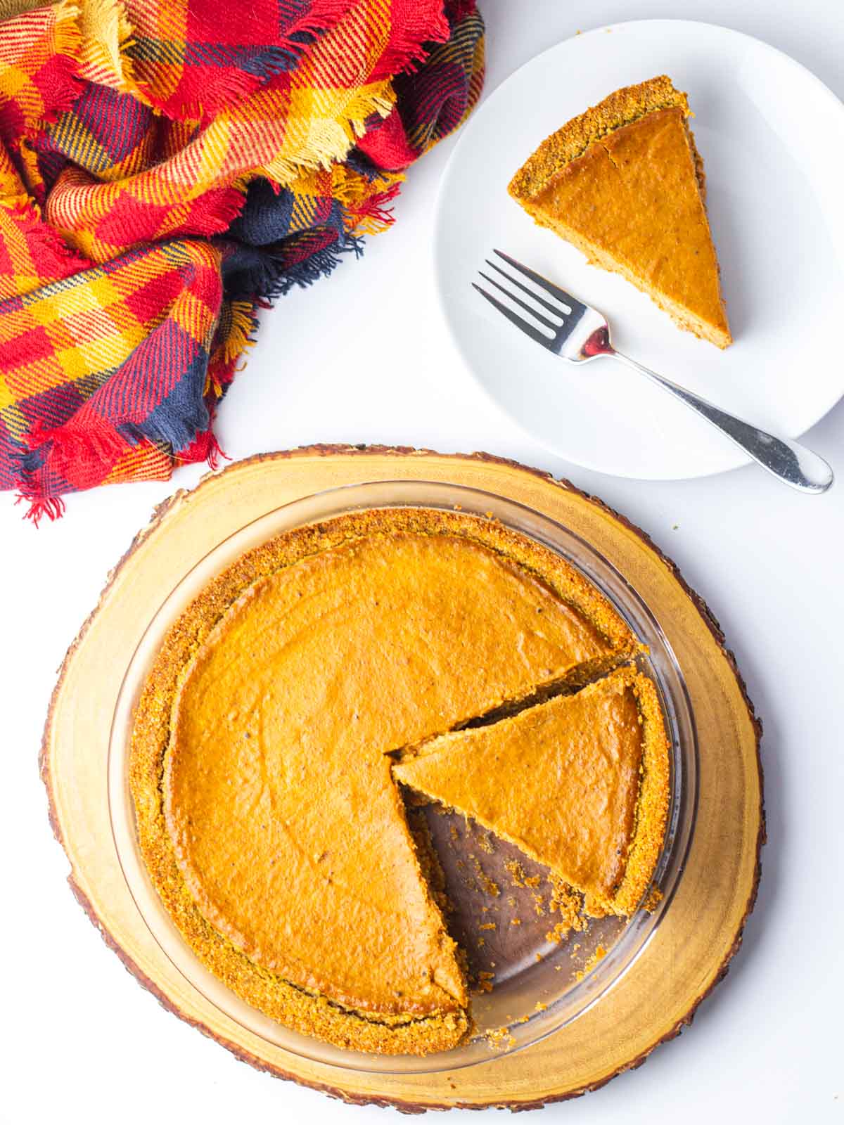 A pumpkin pie with one slice removed on a plate in the upper right corner and a second slice cut but not yet removed.