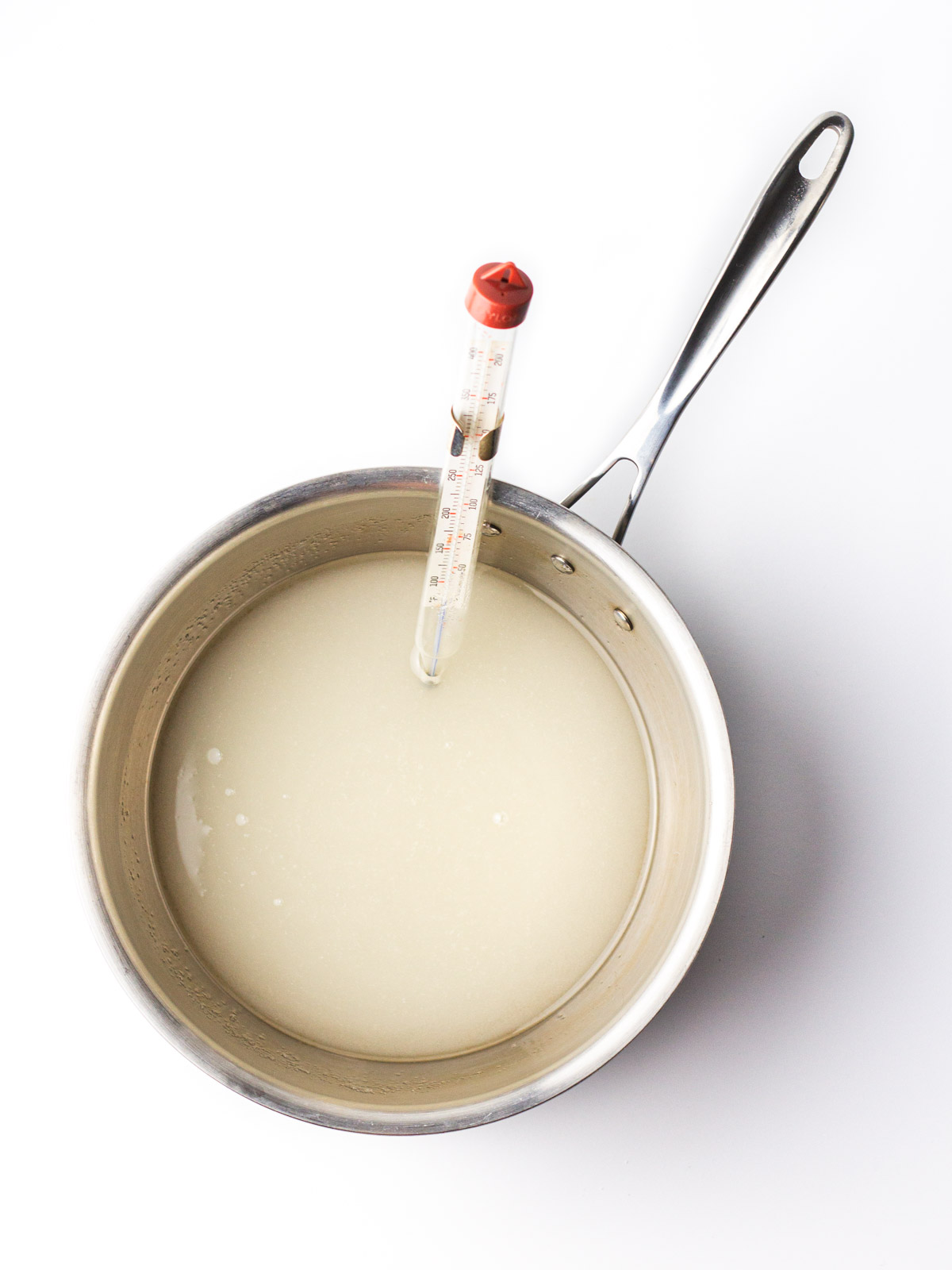 Sugar, corn syrup, and water in a saucepan with a candy thermometer clipped to the side of the pot.
