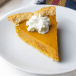 A slice of bourbon pumpkin pie with a dollop of whipped cream on top.
