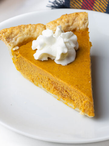 A slice of bourbon pumpkin pie with a dollop of whipped cream on top.