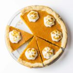 A partially sliced bourbon sweet potato pie with a dollop of toasted meringue on each slice.
