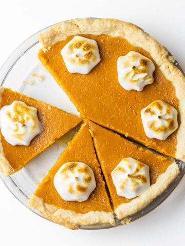 A partially sliced bourbon sweet potato pie with a dollop of toasted meringue on each slice.