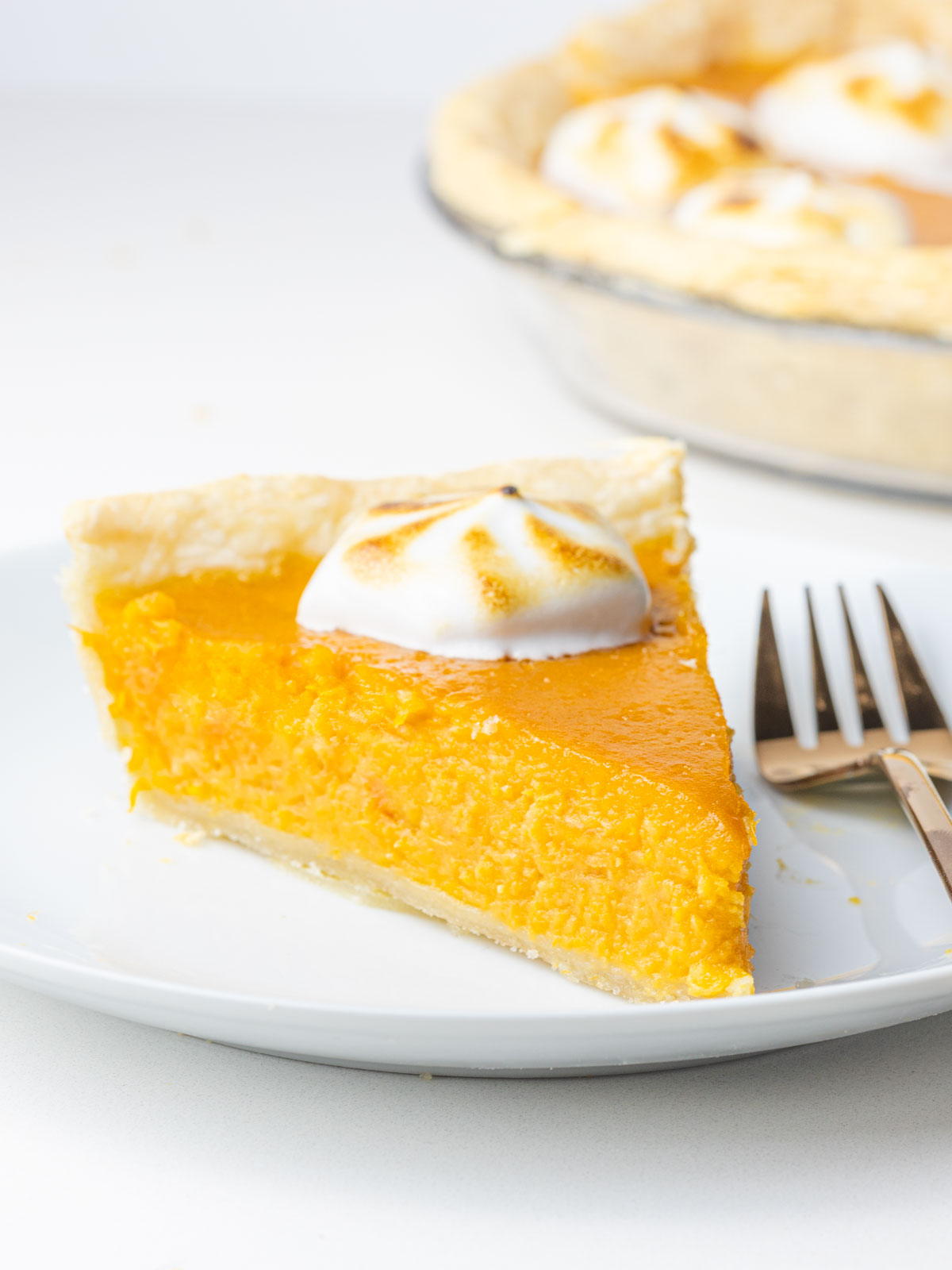 A slice of bourbon sweet potato pie topped with toasted meringue on a plate next to a fork.