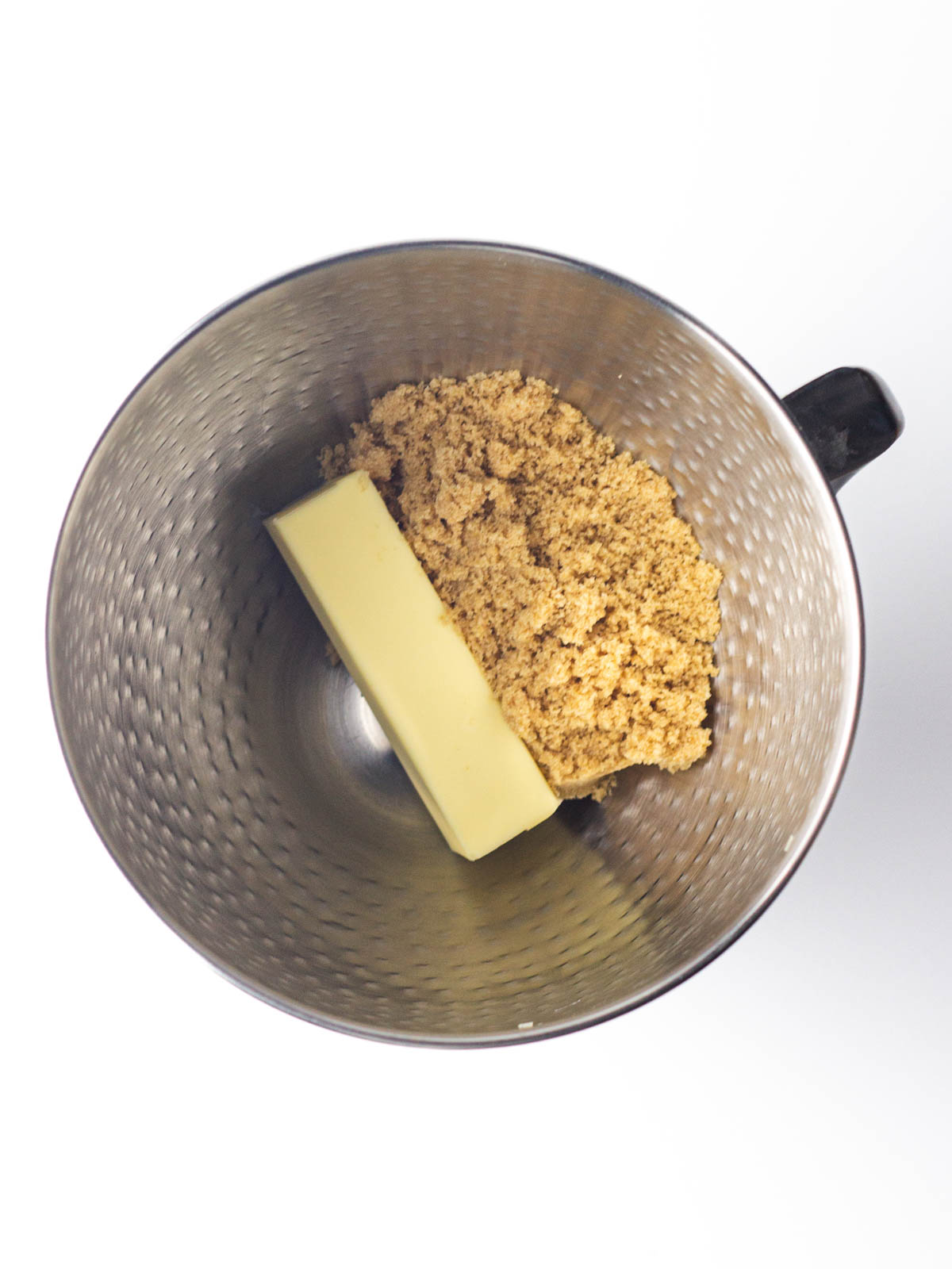 Butter and brown sugar in a silver textured mixing bowl.