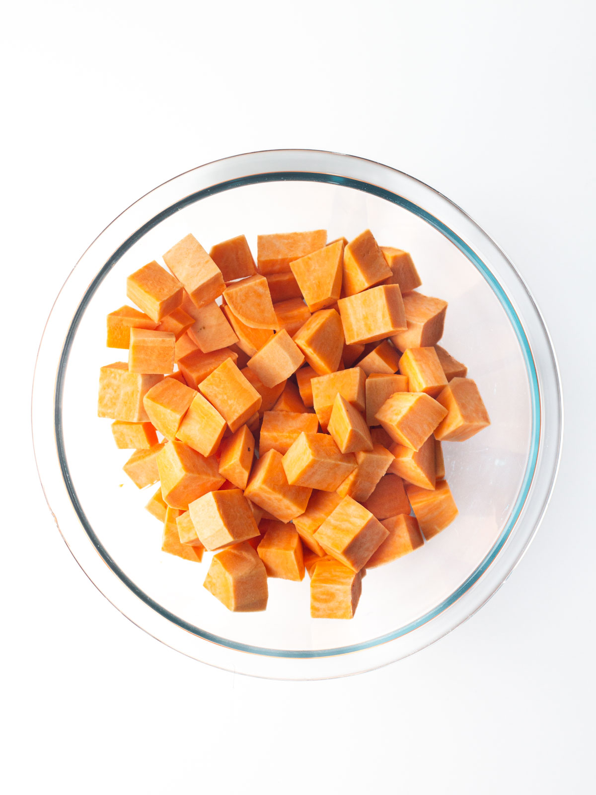 Cubed sweet potatoes in a clear glass mixing bowl.