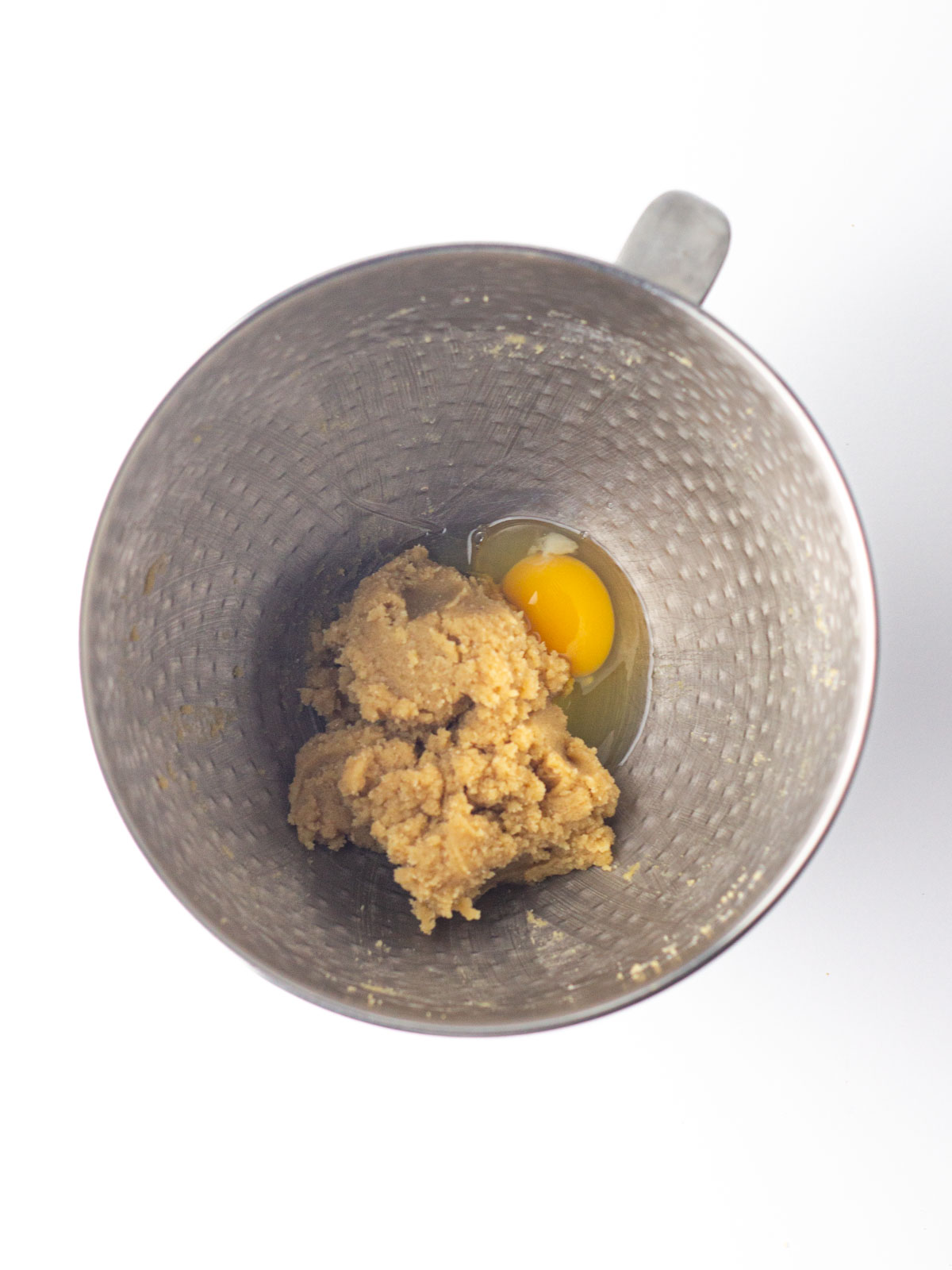 An egg added to creamed butter and brown sugar in a silver textured mixing bowl.