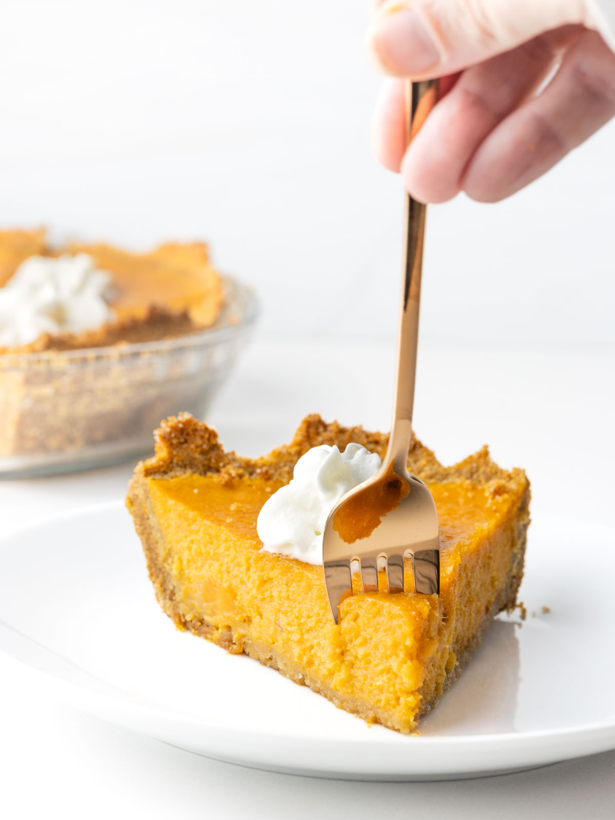 A hand holding a fork into the tip of a slice of sweet potato pie.