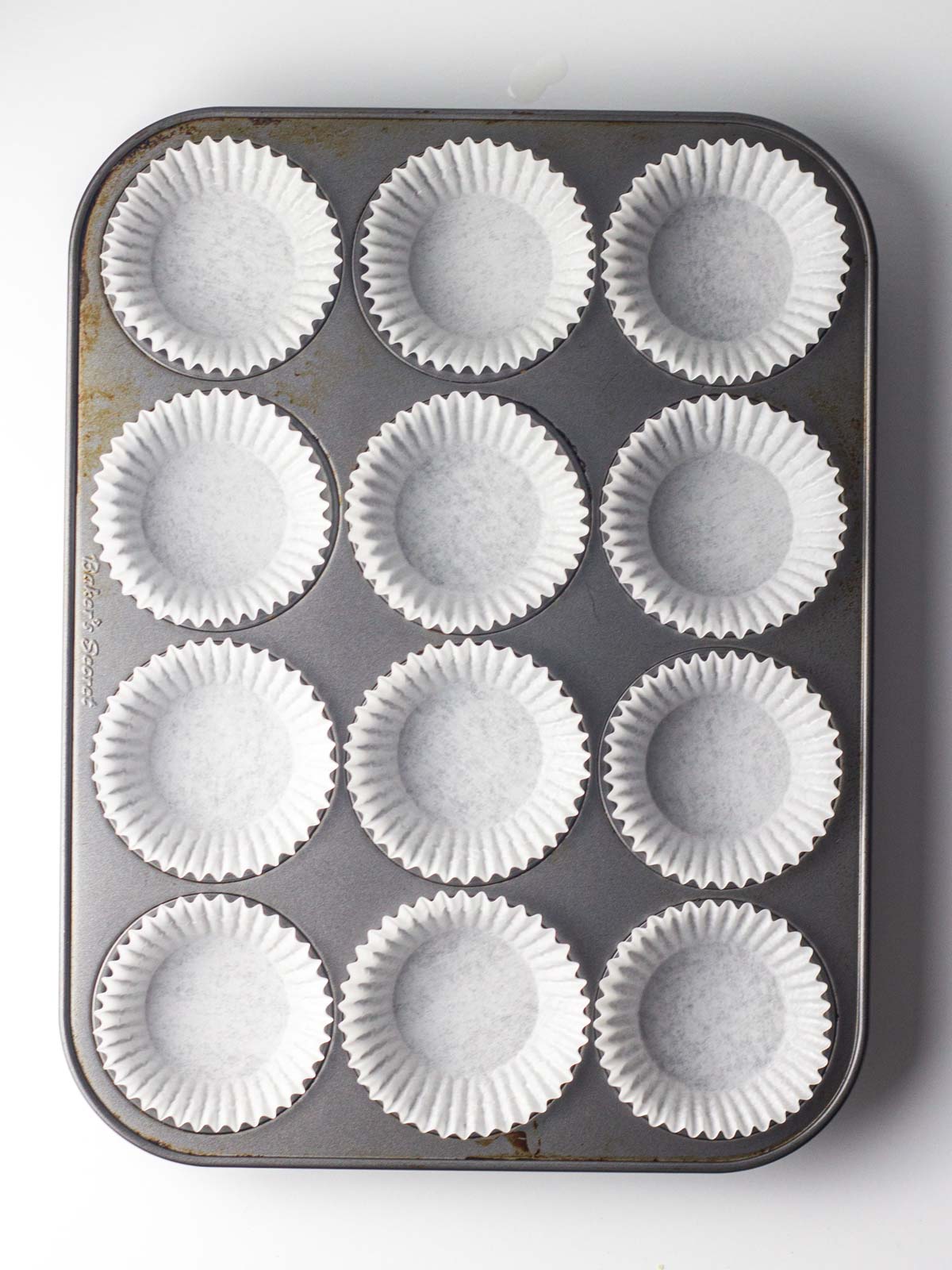 A silver cupcake pan lined with white paper liners.