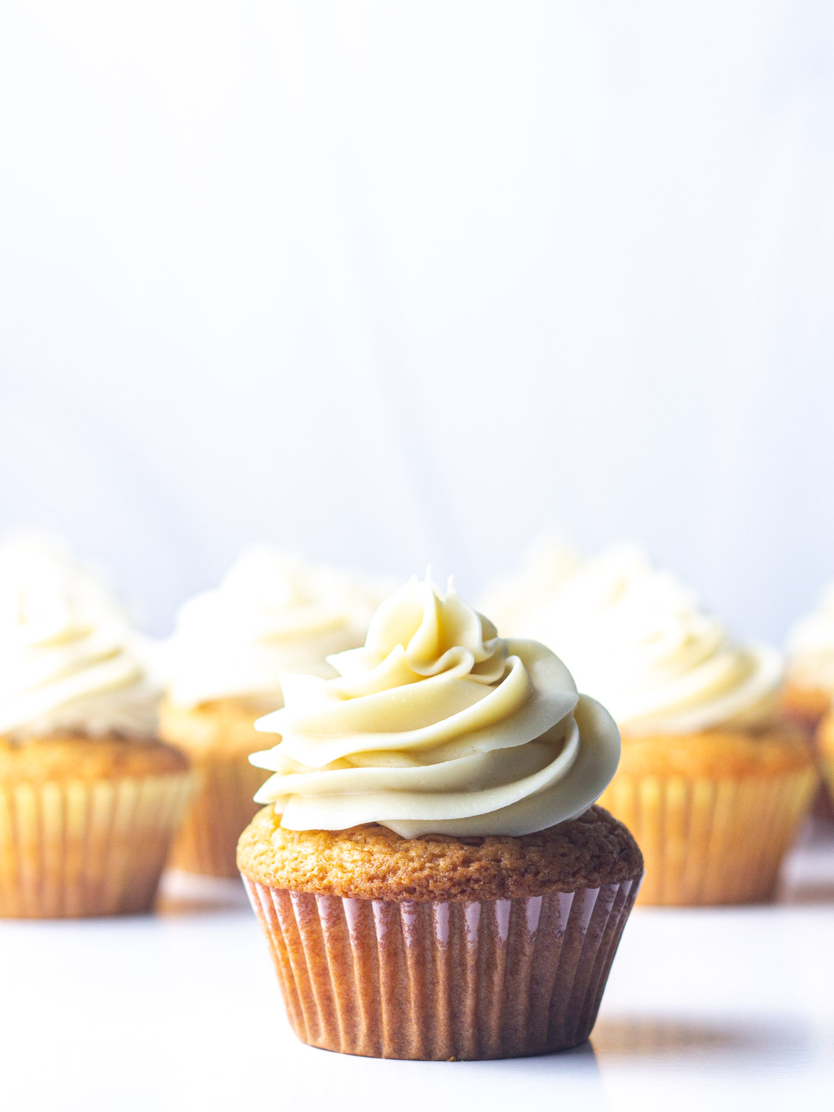 A frosted maple cupcake in front of the rest of the batch of maple cupcakes.