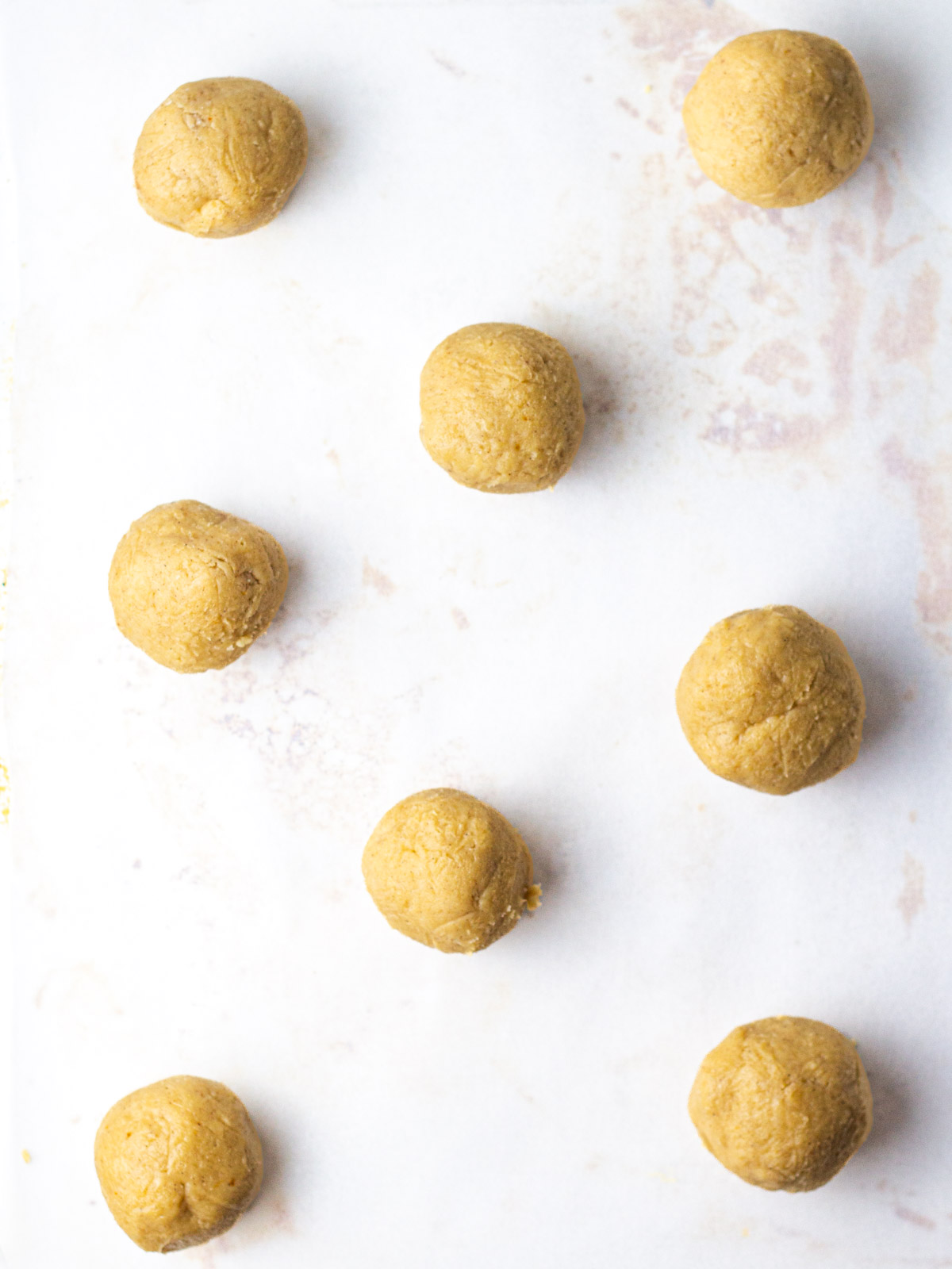 Balls of pumpkin cheesecake cookie dough on a parchment lined baking sheet.