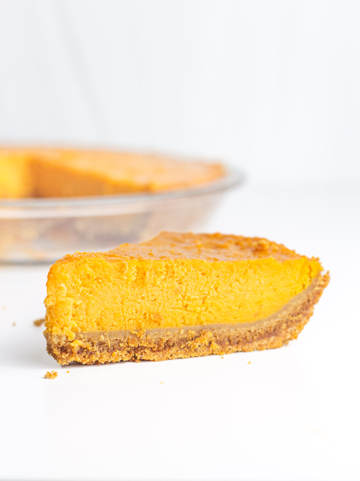 A slice of sweet potato pie on a white surface in front of the rest of the pie in the background.