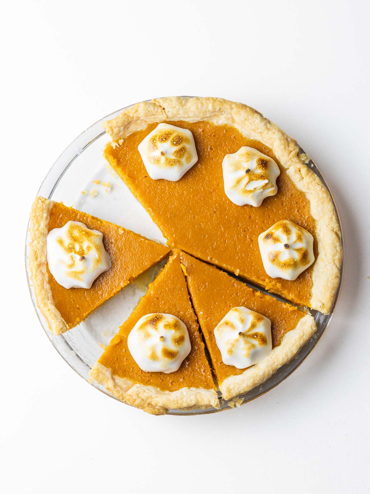 A partially sliced bourbon sweet potato pie with a dollop of toasted meringue on each slice.