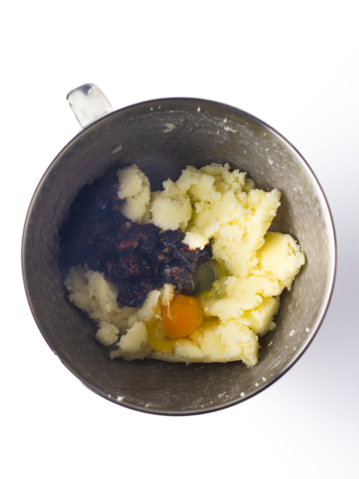 Egg and mashed blueberries added to the creamed butter and sugar in a silver textured mixing bowl.