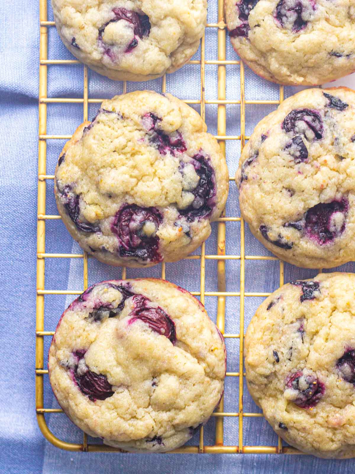 Blueberry cookies on the corner of a gold wire rack on top of a blue linen.