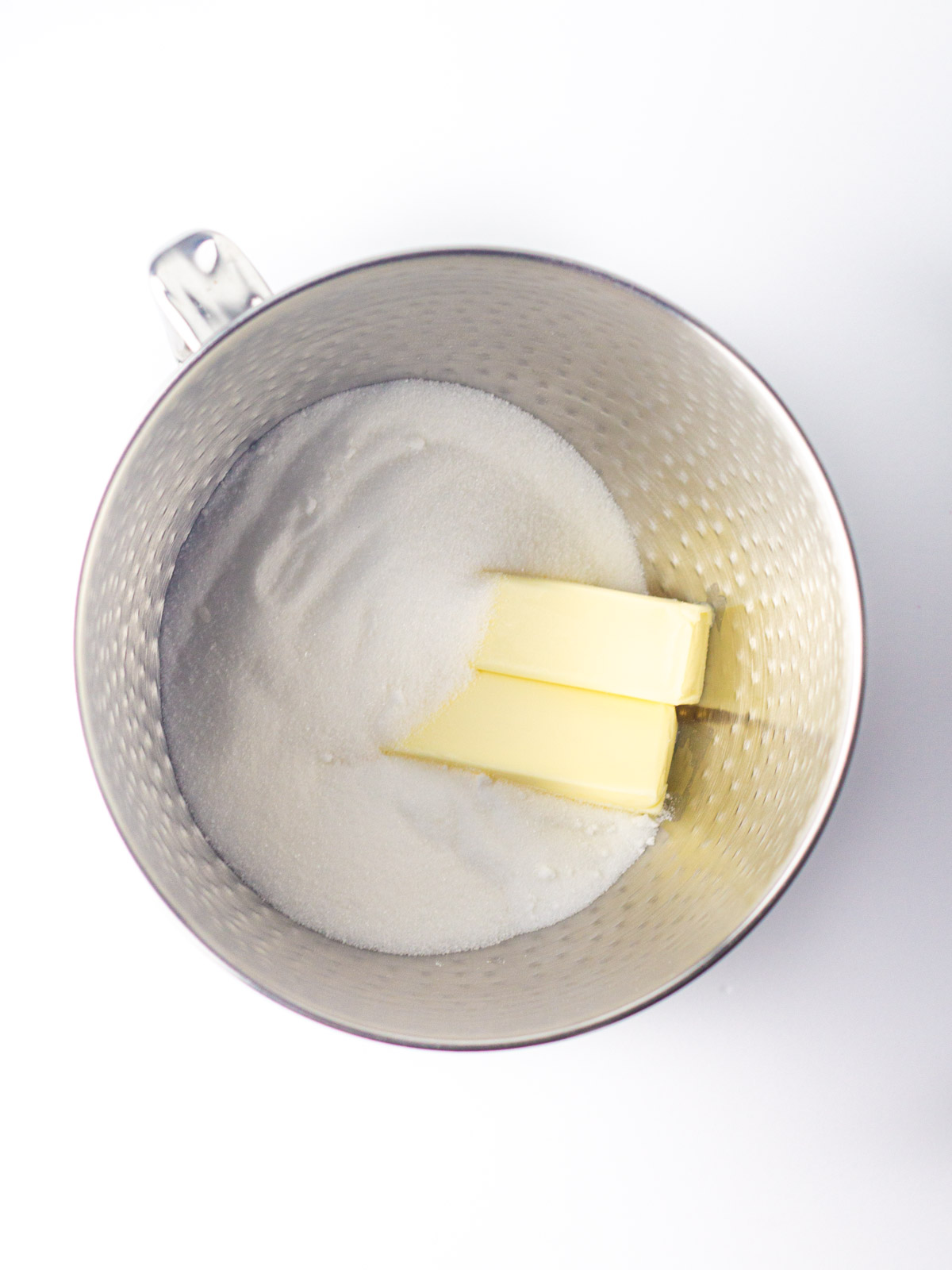 Two sticks of butter and sugar in a silver, textured mixing bowl.