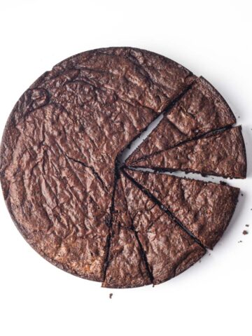 A round flourless chocolate cake with 5 slices cut, but not yet removed from the rest of cake.