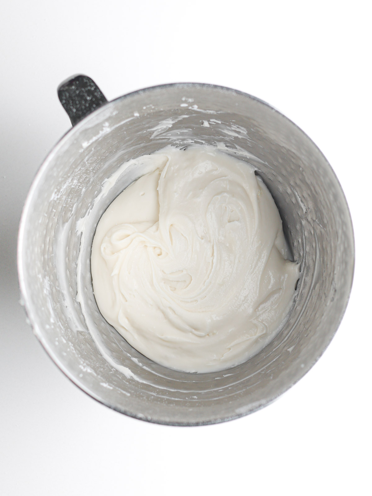 Champagne buttercream frosting in a textured silver metal mixing bowl with a handle.