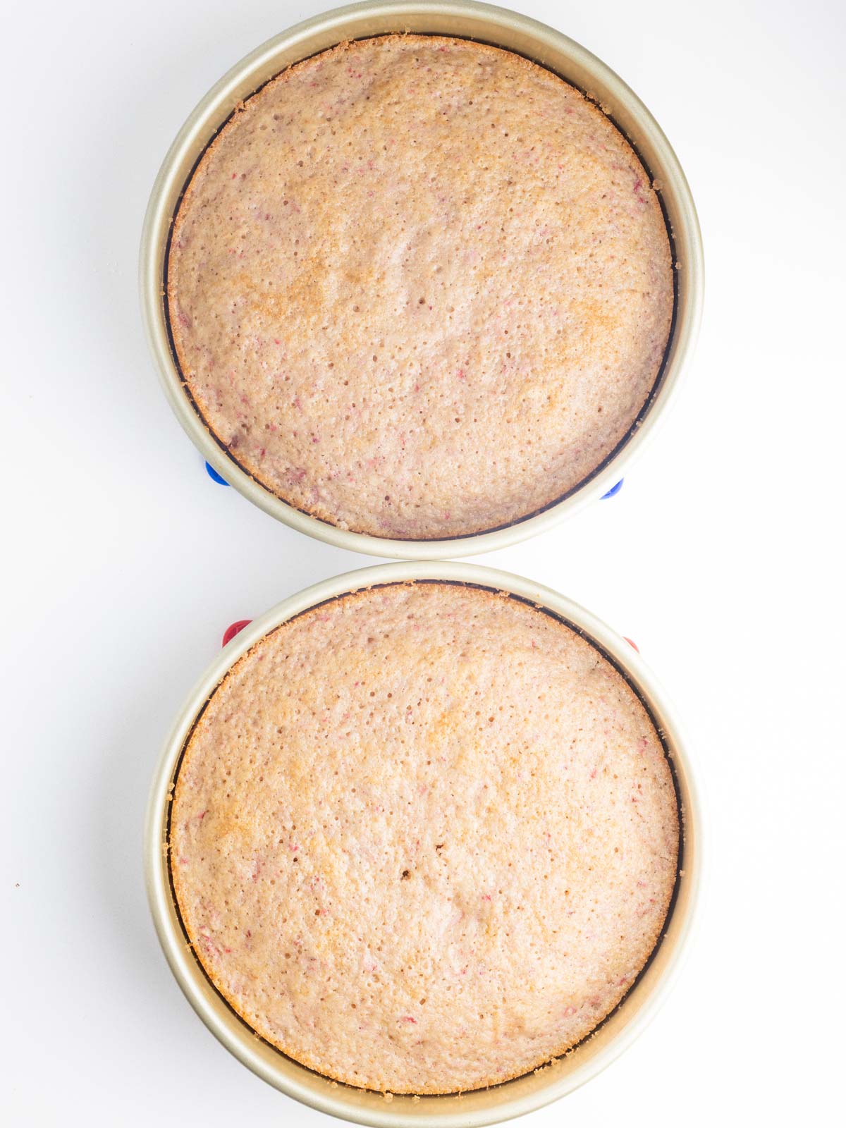 Baked strawberry cake in two cake pans lined up vertically in the frame.