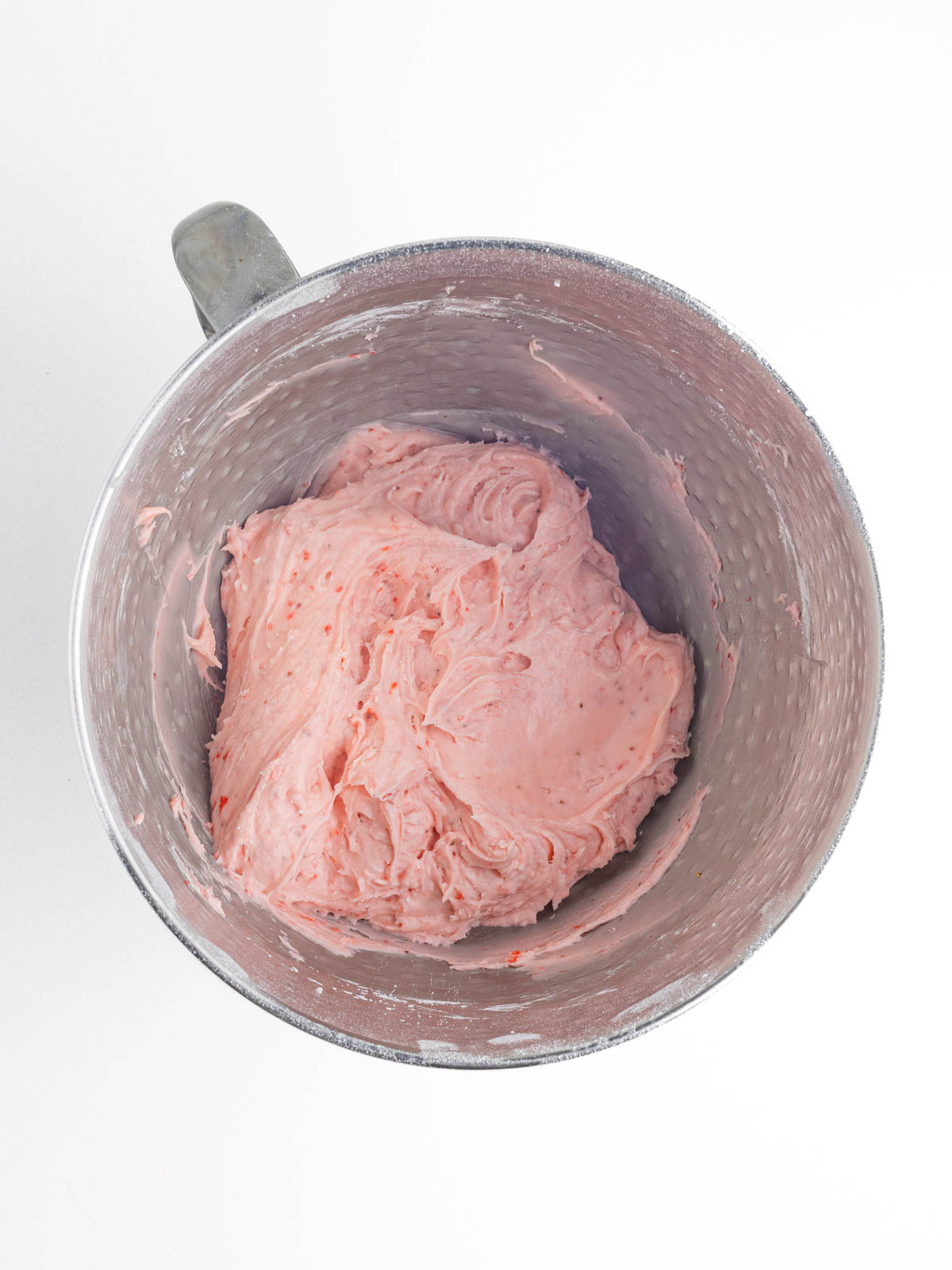 Pink strawberry frosting in a silver textured mixing bowl.