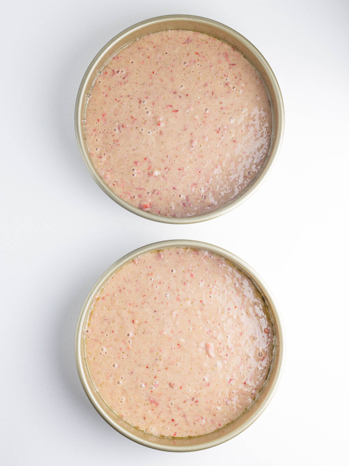 Strawberry cake batter in two cake pans lined up vertically in the frame.