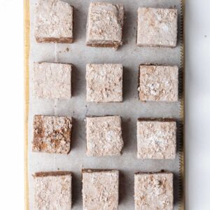 A small wooden cutting board with rows of marshmallows on parchment paper on top.