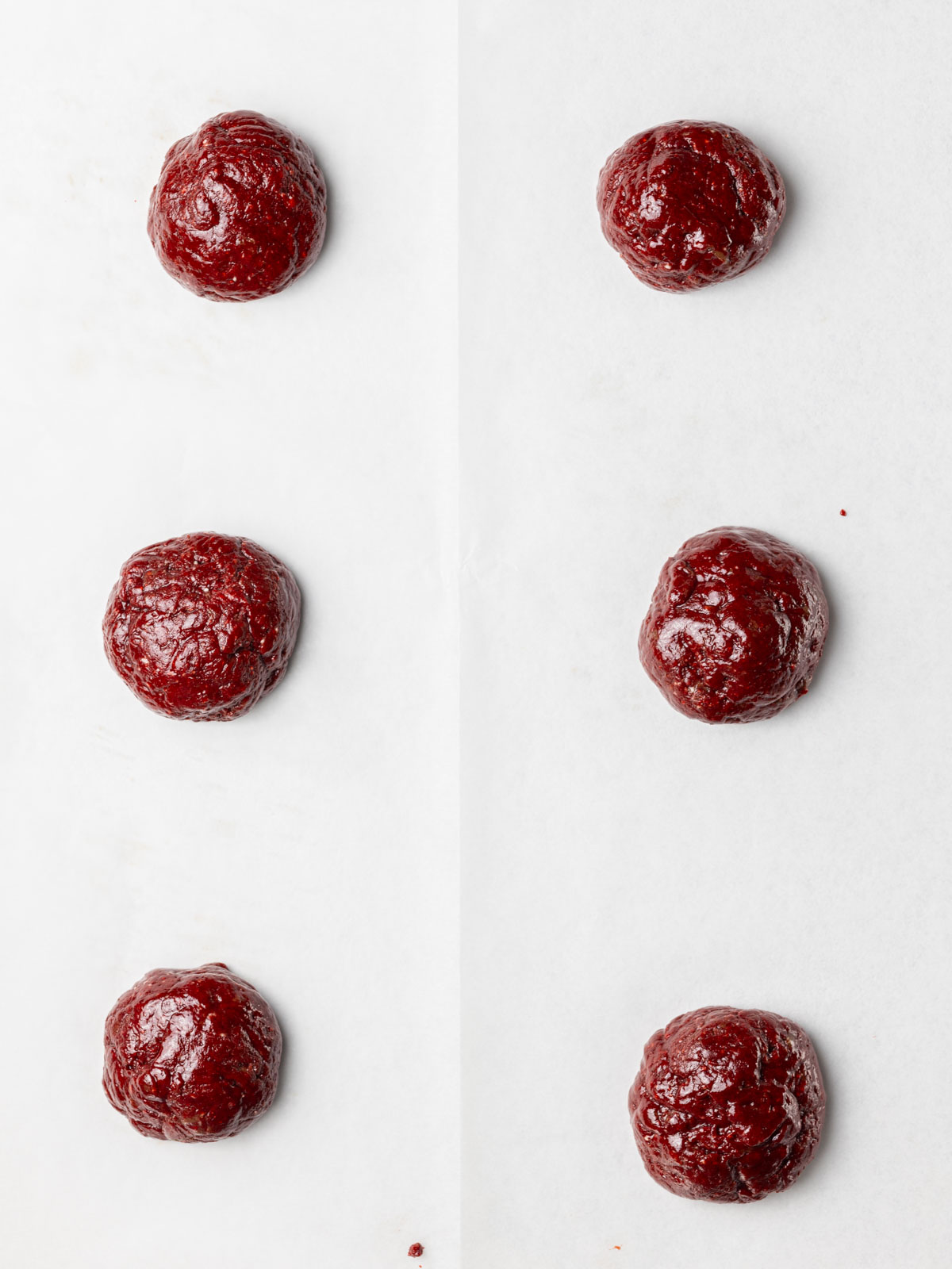 Balls of red velvet cookie dough on a parchment lined baking sheet.