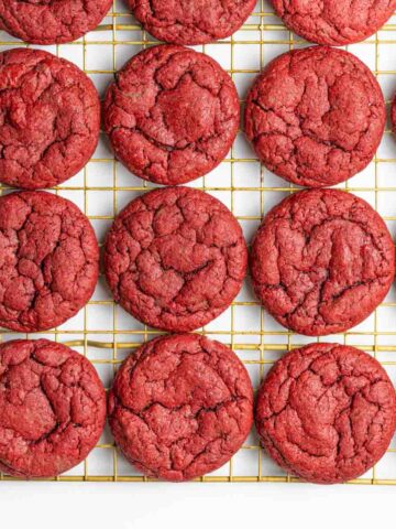 A batch of red velvet cookies on a gold wire rack going out of frame to the top right.