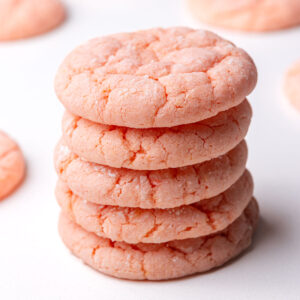 A stack of strawberry cake mix cookies surrounded by more cookies in the background.