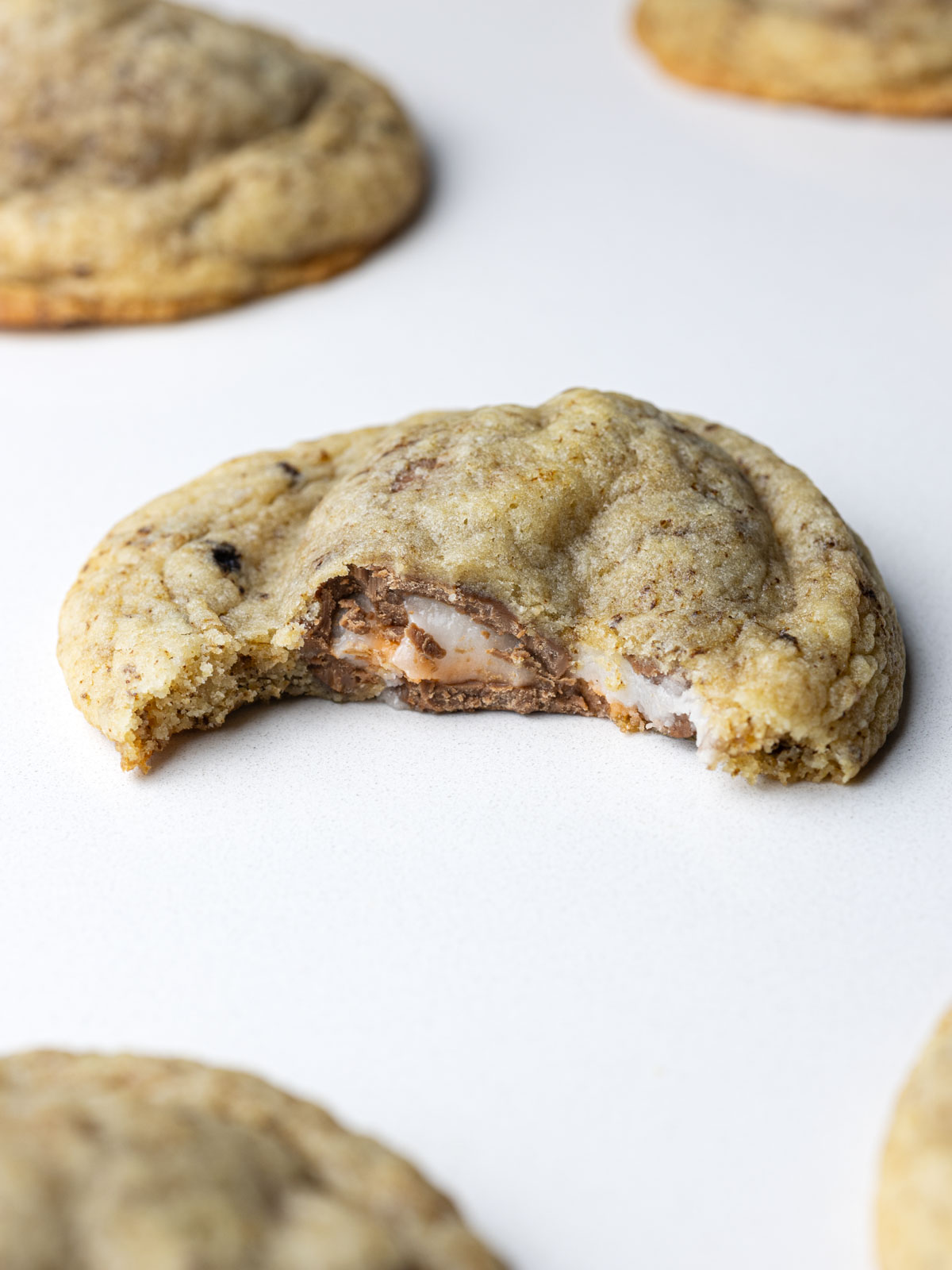 A creme egg cookie with a bite taken out of it on a white surface with other cookies going out of frame all around it.