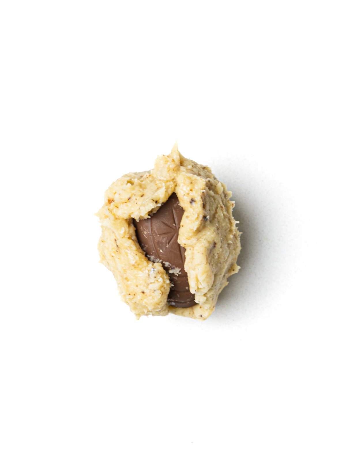 Cookie dough partially wrapped around a creme egg sitting on a white surface.