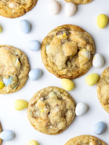 A batch of mini egg cookies on a white surface surrounded by mini eggs.